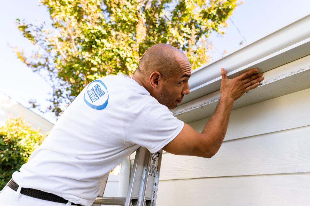 man on latter looking at gutters